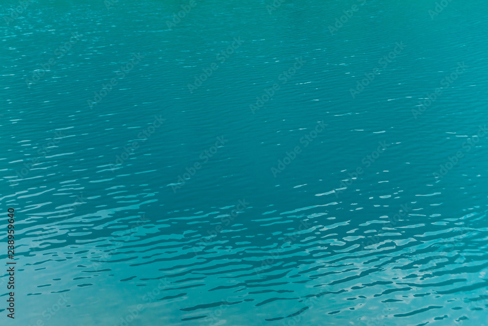 Shiny texture of azure surface of mountain lake. Minimalist background with reflection of mountains in clear water in sunny day. Copy space. Shiny texture of azure surface of mountain lake. Minimalist background with reflection of mountains in clear water in sunny day. Copy space.