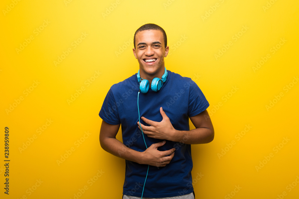 African american man with blue t-shirt on yellow background smiling a lot while putting hands on chest