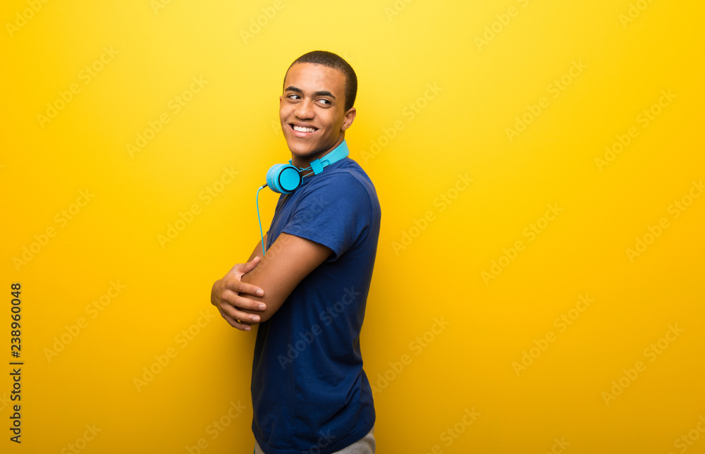 African american man with blue t-shirt on yellow background looking over the shoulder with a smile African american man with blue t-shirt on yellow background looking over the shoulder with a smile