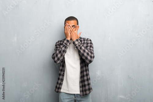 Young african american man with checkered shirt covering eyes by hands and looking through the fingers