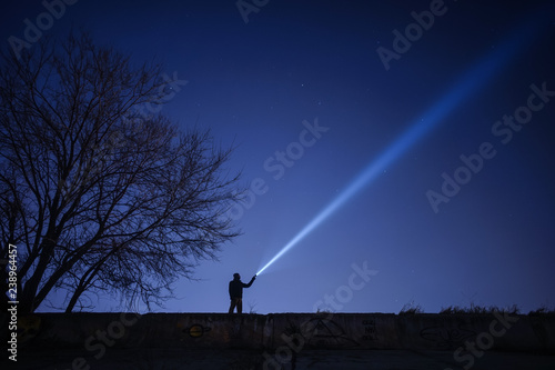 Man pointing flashlight to sky at night. 