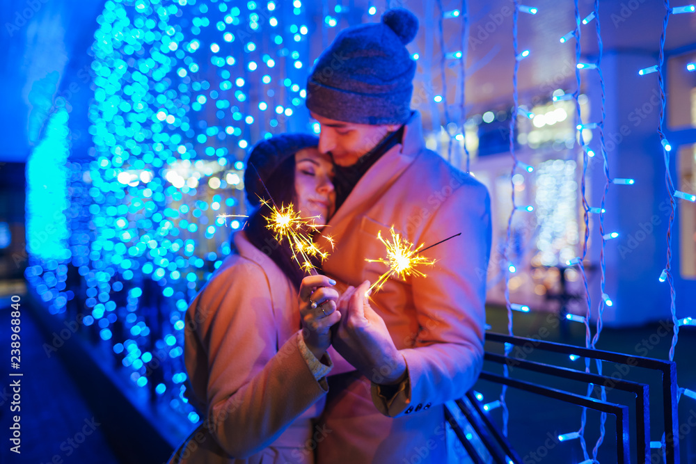 Young loving couple burning sparklers by holiday illumination Young loving couple burning sparklers by holiday illumination