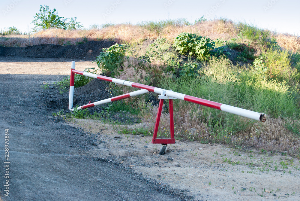Metal barrier of red and white color, prohibition of travel on the road, against the background of a path of green trees and grass, spring rest way Metal barrier of red and white color, prohibition of travel on the road, against the background of a path of green trees and grass, spring rest way