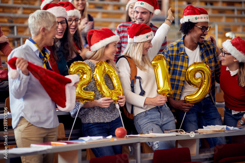 Smiling Students in Santa hat holding 2019 golden balloons at New Year party .