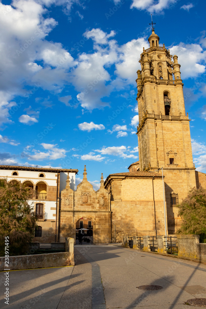 View of the old Gate of Castile, Puerta de Castilla and the tower of Church of Santa Maria in Los Arcos, Navarre Spain against a beautiful blue sky with fluffy white clouds