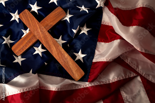 Evangelical America, christianity, born again christian and fundamentalist religious right concept with close up on a wooden cross or crucifix on the american flag with dramatic light and moody tone photo