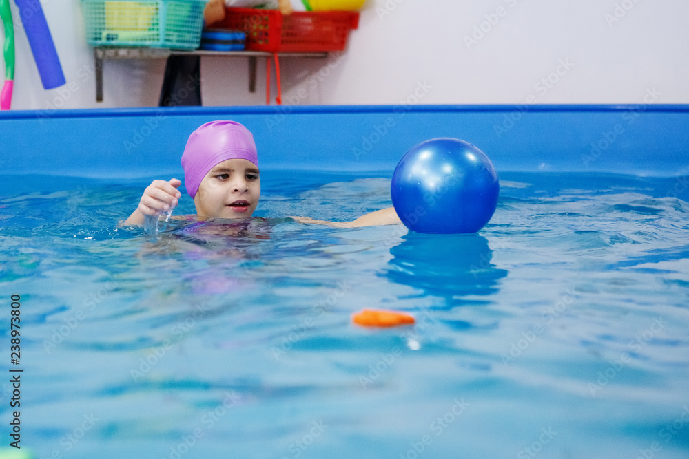 Girl in the lilac hat is having fun, swimming in the pool.