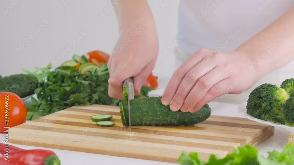 A woman in the kitchen chops a cucumber, prepares a delicious fresh vegetable salad for lunch A woman in the kitchen chops a cucumber, prepares a delicious fresh vegetable salad for lunch