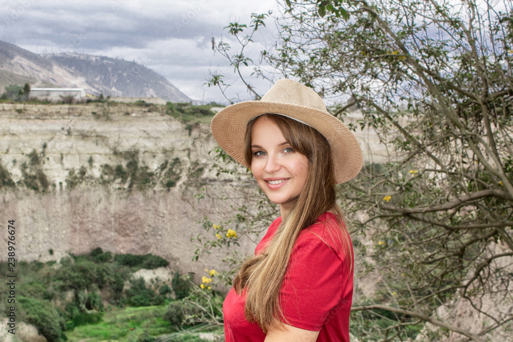 Portrait. A beautiful young woman in a hat and red dress is sitting on the edge of a mountain and admiring the scenery.