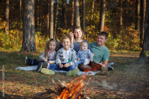 Family father, mother, two boys and girl by the fire in autumn forest.