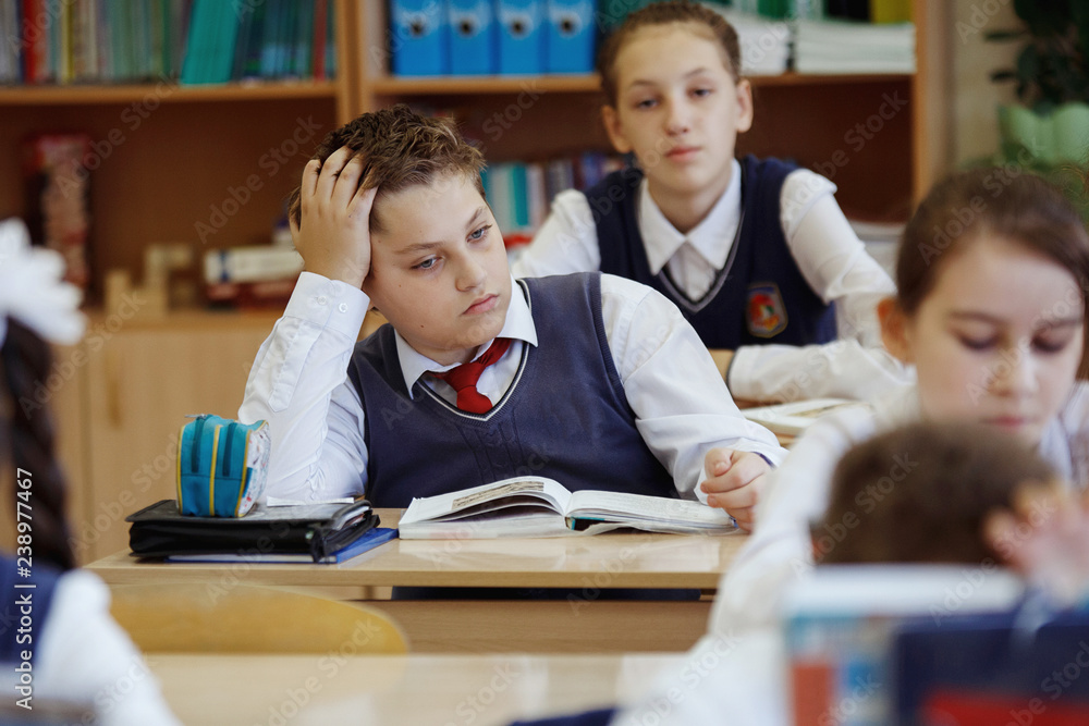 A young schoolboy sitting at a desk in a school class. A young schoolboy sitting at a desk in a school class.
