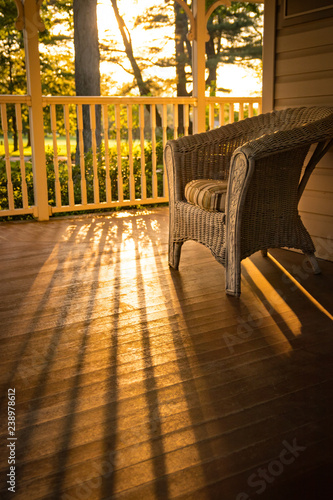 Photography Warm sunny view of home: a wicker chair on wooden porch.