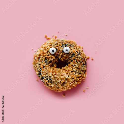 Funny shock face chocolate peanut donut on a pastel pink background, creative minimal Halloween concept
