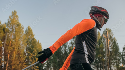 Training an athlete on the roller skaters. Biathlon ride on the roller skis with ski poles, in the helmet. Autumn workout. Roller sport. Adult man riding on skates. photo