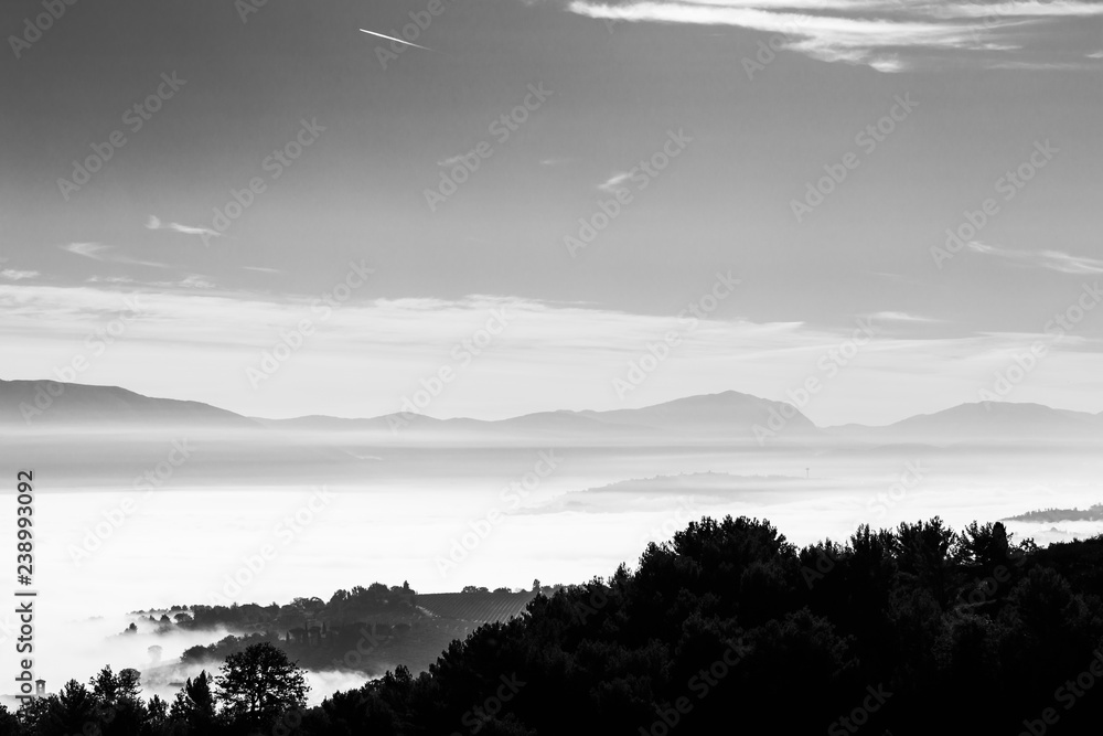Fog filling a valley in Umbria (Italy), with layers of mountains and hills and trees in the foreground Fog filling a valley in Umbria (Italy), with layers of mountains and hills and trees in the foreground