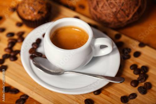 A Cup of fragrant espresso coffee with foam close-up. Coffee in white Cup and coffee beans scattered on wooden background