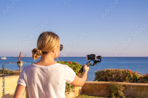 Attractive female records video with modern 3d gimbal stabilized camera smartphone.