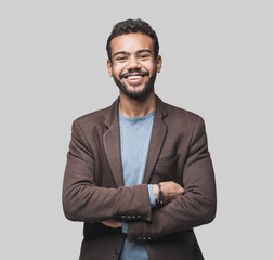 Portrait of handsome smiling young man with folded arms. Laughing joyful cheerful men with crossed hands studio shot. Isolated on gray background