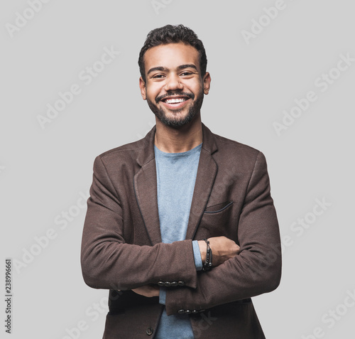 Portrait of handsome smiling young man with folded arms. Laughing joyful cheerful men with crossed hands studio shot. Isolated on gray background photo