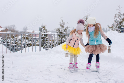 Adorable girls skating on ice rink outdoors in winter snow day
