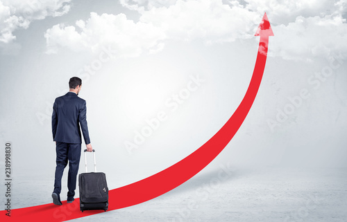 Young businessman with back leaving on the red arrow carpet to the skies with luggage on his hand 