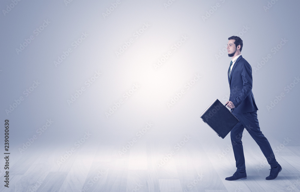Successful businessman walking in front of an empty wall with briefcase on his hand
Successful businessman walking in front of an empty wall with briefcase on his hand