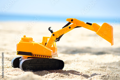 bulldozer toy  ,dig machine toy  with sun light on the beach ,blue background.