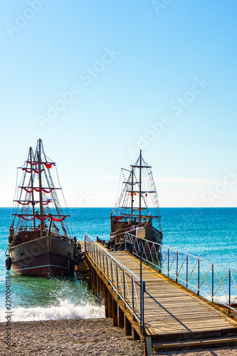 Two wooden sailing ships at the wooden pier against the blue sea on a bright sunny afternoon