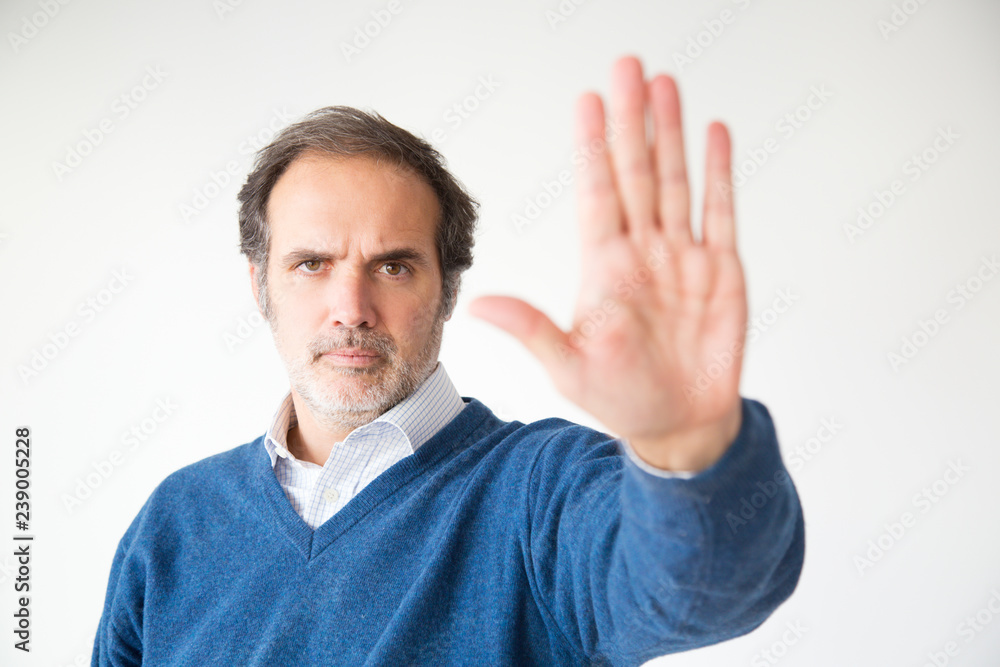 Serious middle aged man gesturing stop sign. Handsome mature man with grey hair gesturing forbidden with hand. Isolated on white. Prohibition concept Serious middle aged man gesturing stop sign. Handsome mature man with grey hair gesturing forbidden with hand. Isolated on white. Prohibition concept