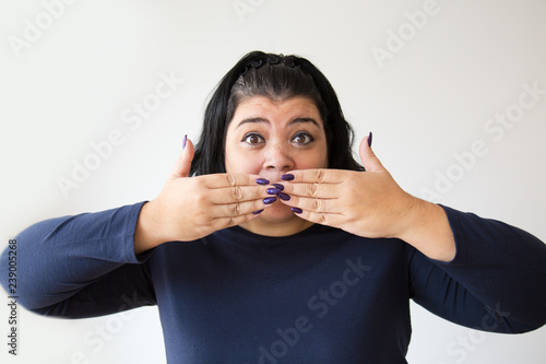 Shocked Hispanic overweight woman covering mouth with teo hands. Stressed woman looking at camera. Isolated on white. Shock concept
