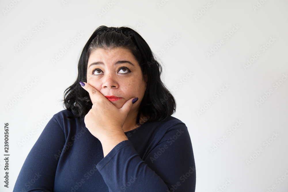 Thoughtful overweight woman holding chin and looking up, studio portrait. Pensive Latin woman in casual clothing. Isolated on white. Thinking concept Thoughtful overweight woman holding chin and looking up, studio portrait. Pensive Latin woman in casual clothing. Isolated on white. Thinking concept