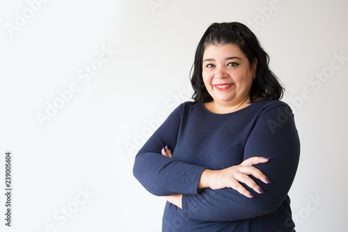 Successful overweight Hispanic woman posing with crossed arms. Smiling adult plus size woman looking at camera. Isolated on white. Success concept photo