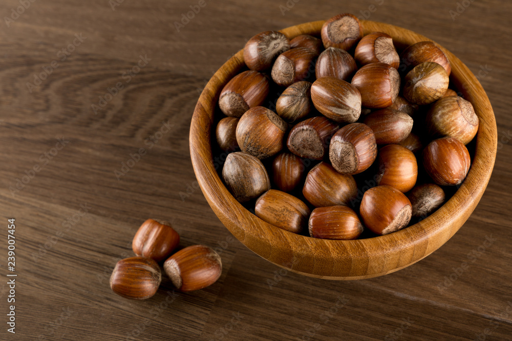 Hazelnuts in wooded bowl isolated on wood background, top view, copy space Hazelnuts in wooded bowl isolated on wood background, top view, copy space