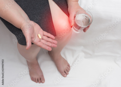 A woman with a sore knee holds a chondroprotector tablet and a glass of water, glucosamine and chondroitin sulfate in her hand, copy space photo