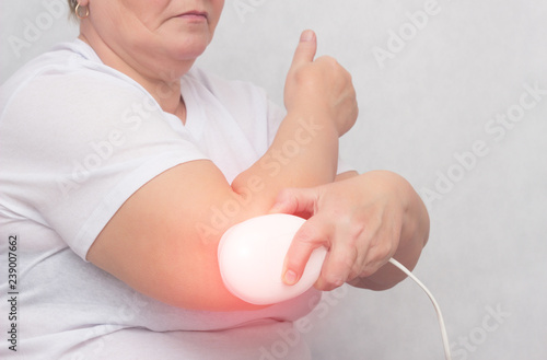 An adult woman treats the elbow joint with a magnetic field, relieves pain and inflammation with a medical magnet, physiotherapy, copy space