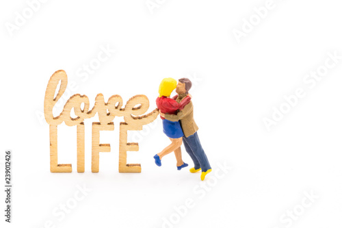 Miniature figures as in love hugging couple next to wooden sign with text Love Life, isolated on white background