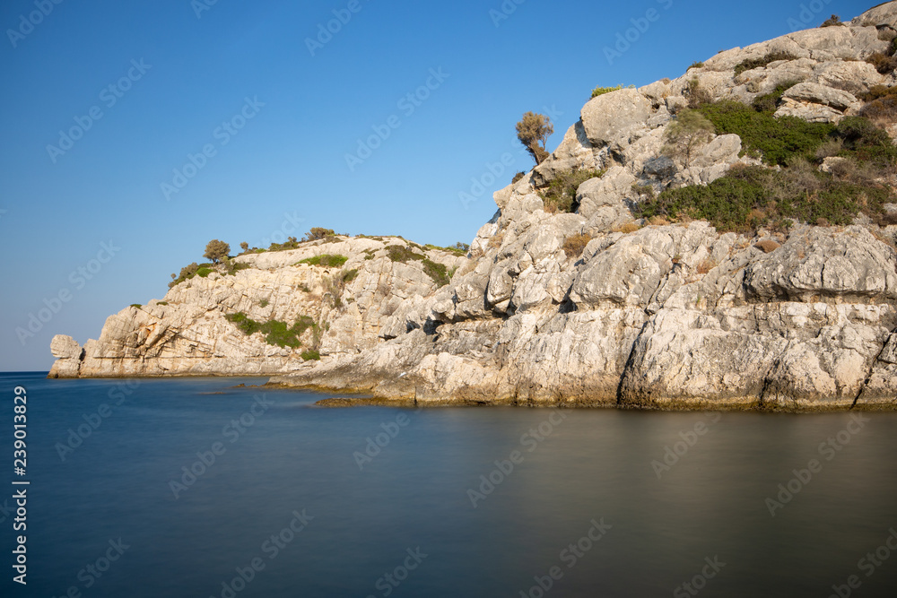 Felsklippen in der Bucht von Kolymbia mit spiegelglattem Wasser im Vordergrund