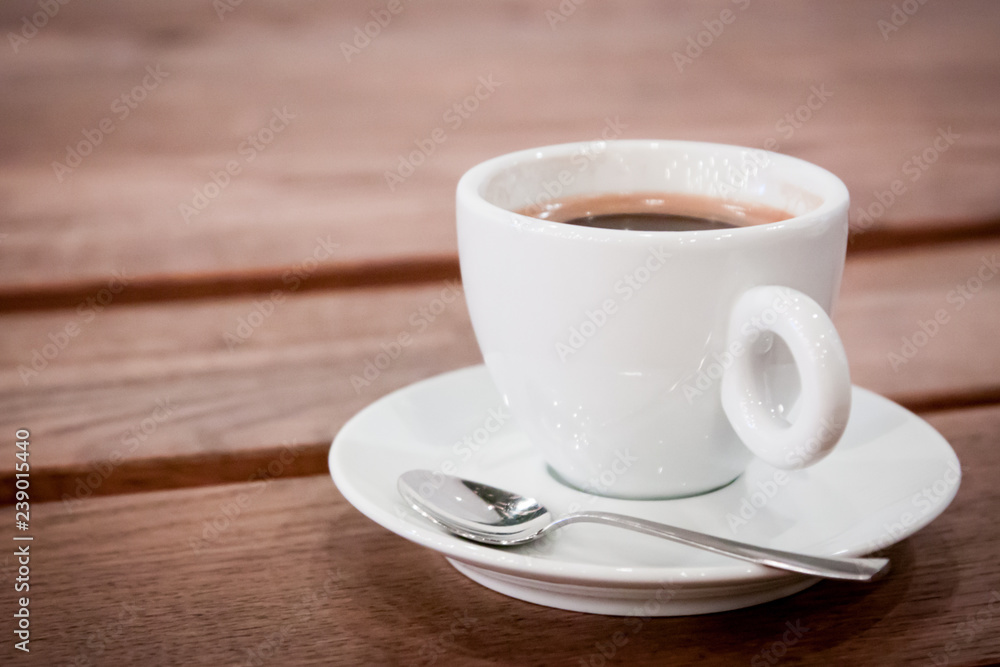 a cup of coffee on a saucer and a spoon stands on a wooden table. aromatic hot fresh coffee. wooden vintage table background with diagonal lines. for design and decor. selective focus