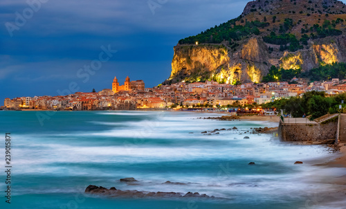 Cefalu town on the coast of Sicily island with blurry sea surface and illuminated mountain in Sicily island, Italy photo