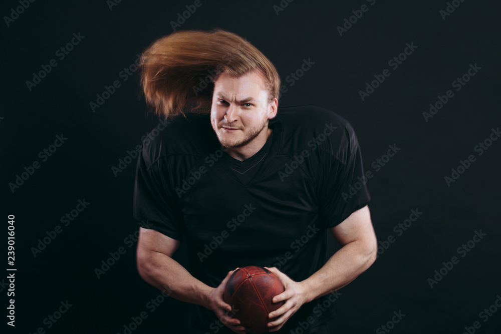 Naklejka premium Healthy american football goalkeeper holding ball in arms looking at camera with cheerful and confident expression posing isolated on black background