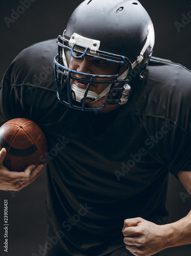 Handsome caucasian man wearing american football uniform and helmet running in action with a ball over dark background