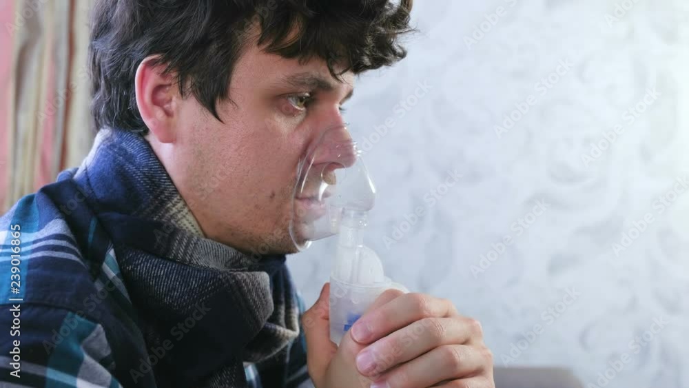Use nebulizer and inhaler for the treatment. Sick man inhaling through inhaler mask. Close-up face, side view. Use nebulizer and inhaler for the treatment. Sick man inhaling through inhaler mask. Close-up face, side view.