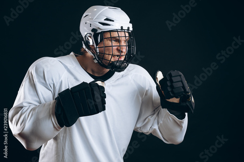 Photography Portrait of professional ice-hockey player in white sportwear, standing in defensive stance looking fierce, isolated over black background