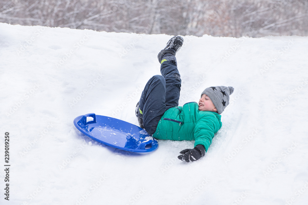 Boy falls rolling down a hill on snow saucer. Winter games