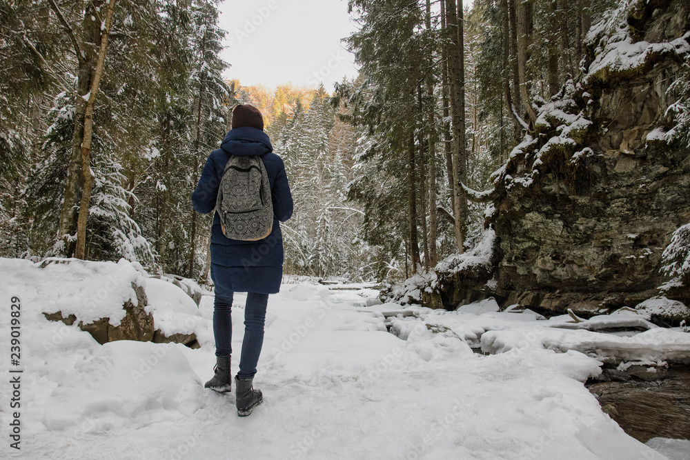 Girl with a backpack is standing a snowy forest. Winter day