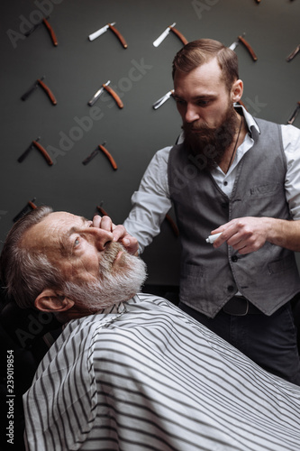 Respectable senior caucasian man visiting hairstylist in barber shop for shaving and making new design for his grey-haired beard