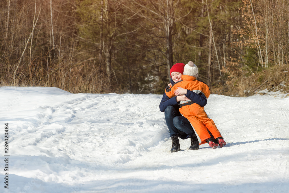 Mum embraces the small son on a background of pine forest. Winter snowy day in the coniferous forest