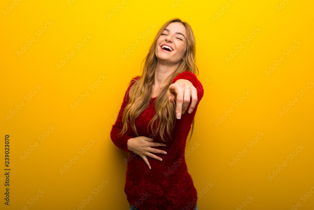 Young girl on vibrant yellow background pointing with finger at someone and laughing a lot Young girl on vibrant yellow background pointing with finger at someone and laughing a lot