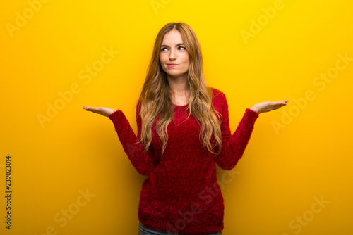 Young girl on vibrant yellow background having doubts while raising hands and shoulders photo
