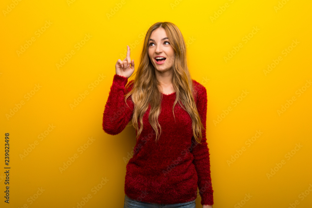 Young girl on vibrant yellow background intending to realizes the solution while lifting a finger up Young girl on vibrant yellow background intending to realizes the solution while lifting a finger up